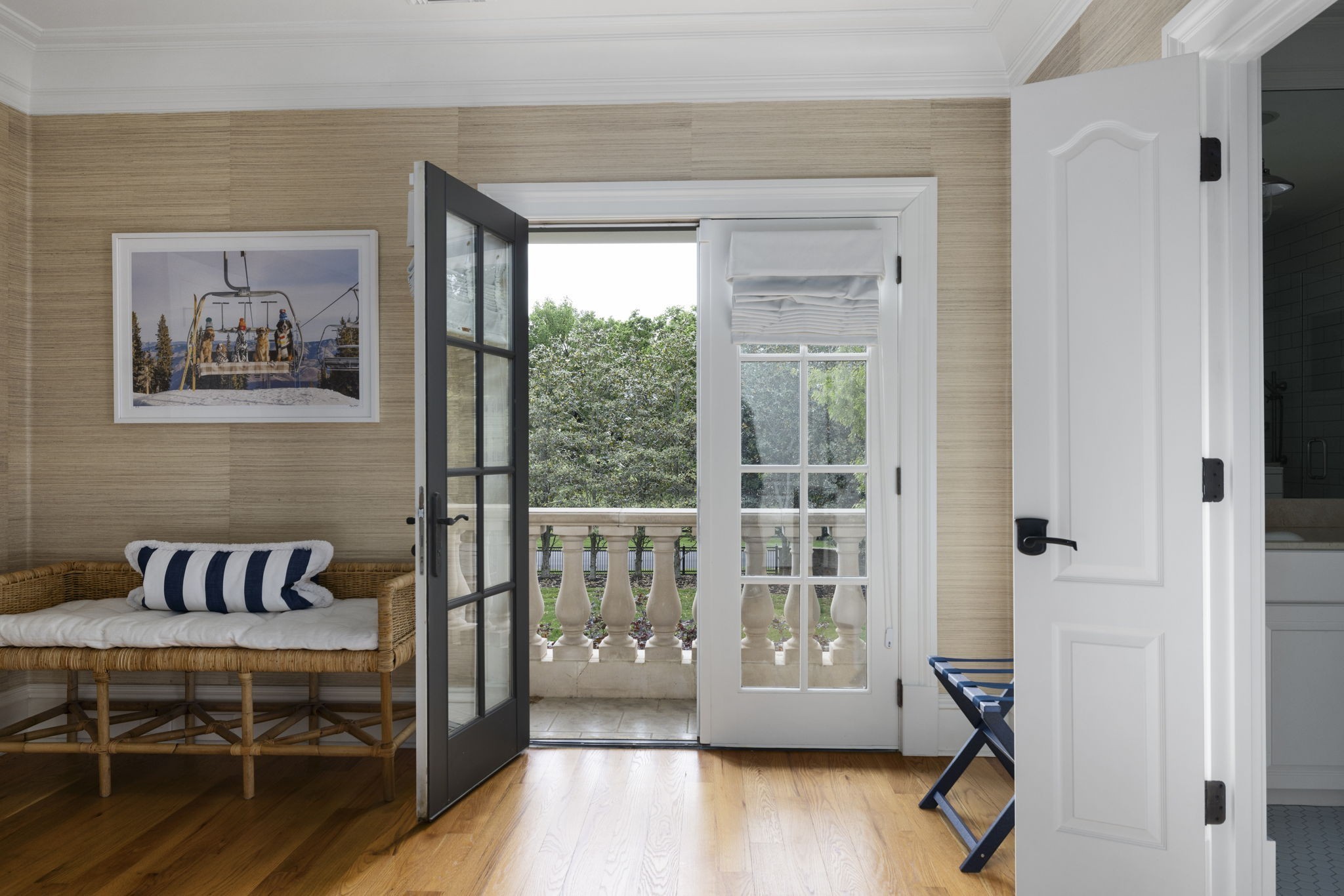 Furnished sitting area with a wicker bench and open doors to a terrace overlooking leafy trees.