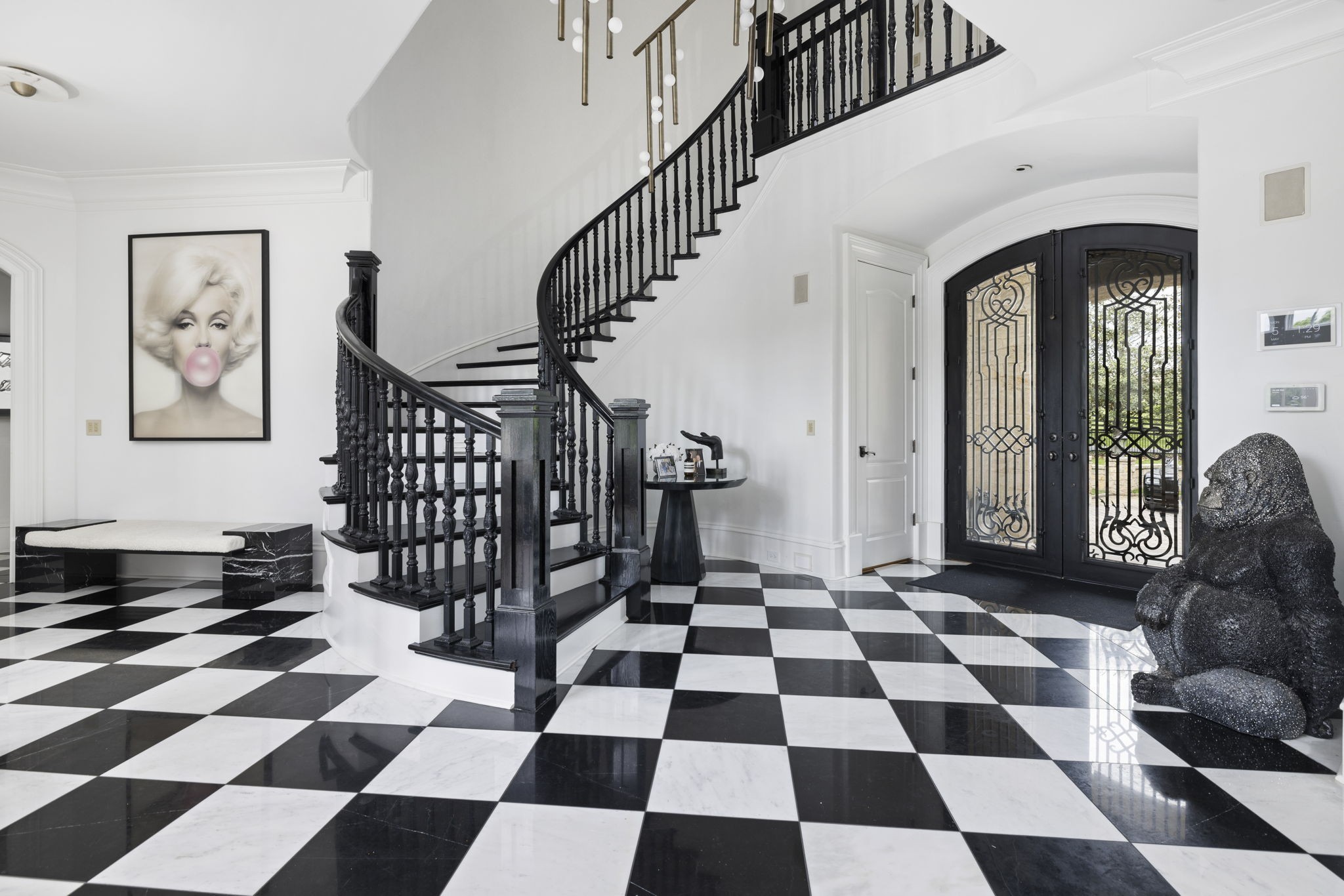Foyer with a curved black staircase, checkerboard floor, ornate double doors, and a large gorilla sculpture.