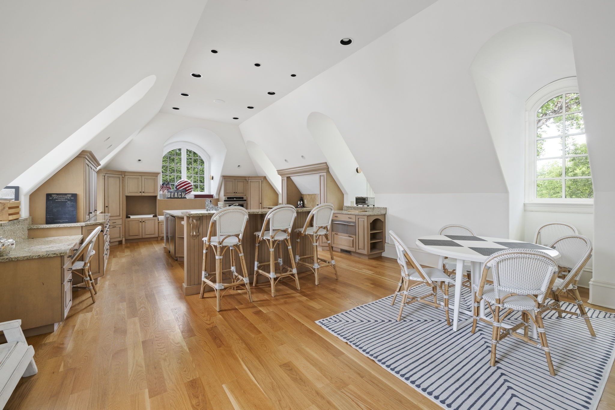 Kitchen and dining area with a central island, light wood cabinetry, and tall arched windows.