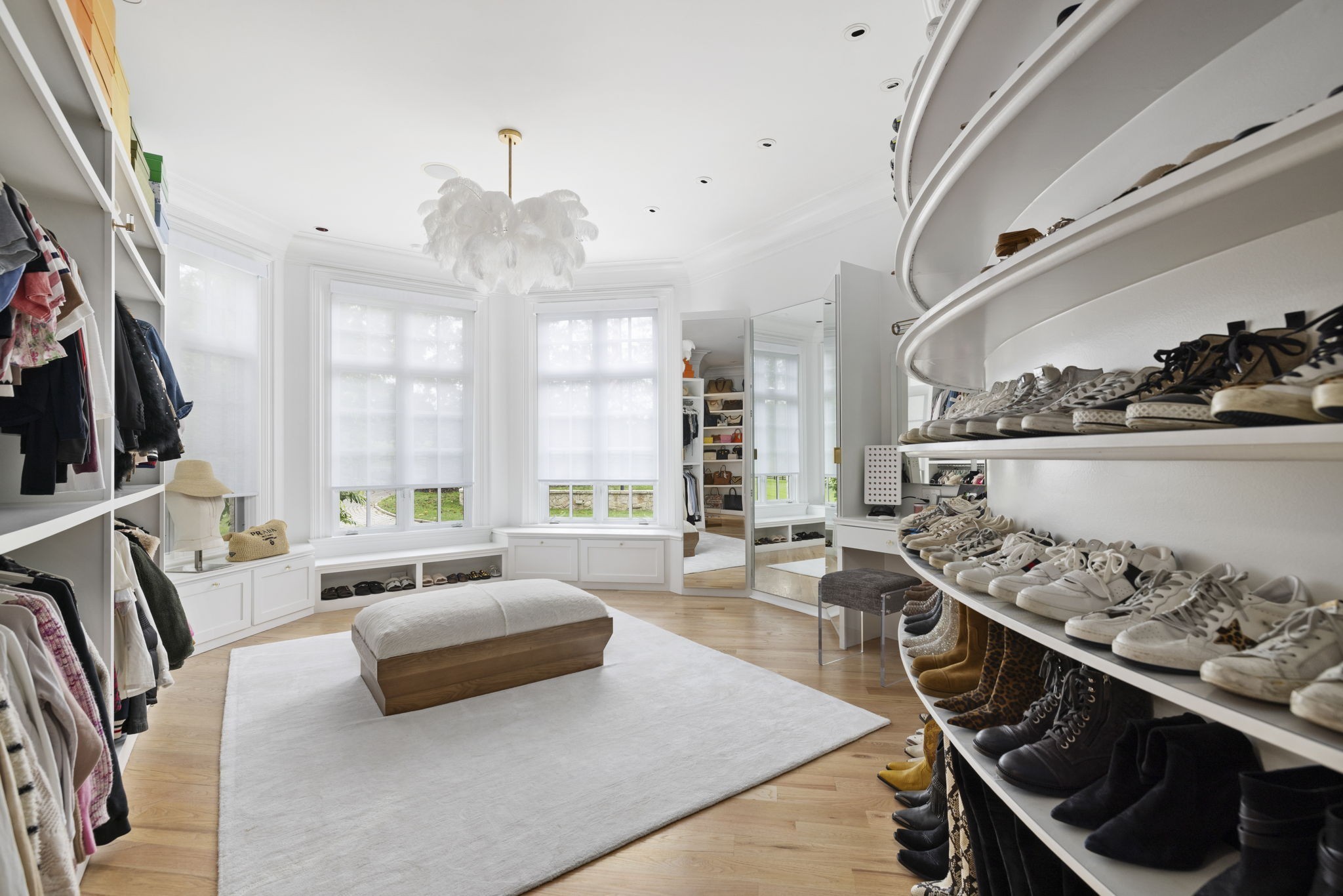 Walk-in closet with curved shoe shelves, bright bay windows, and a padded ottoman.