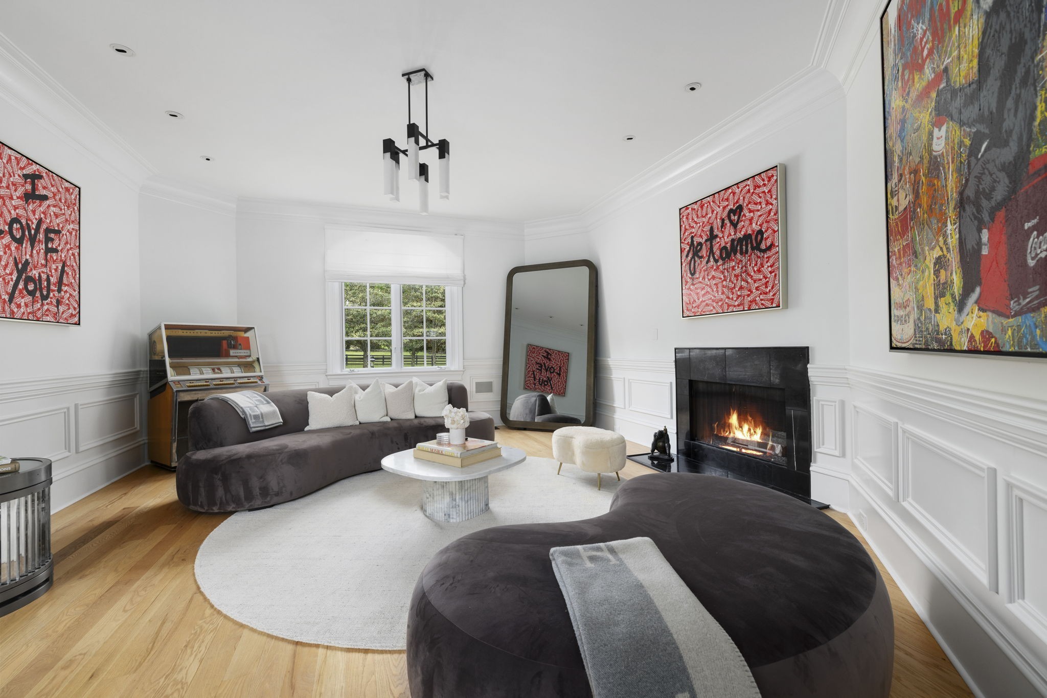 Living room with curved dark sofas, a lit fireplace, vintage jukebox, and colorful wall art.