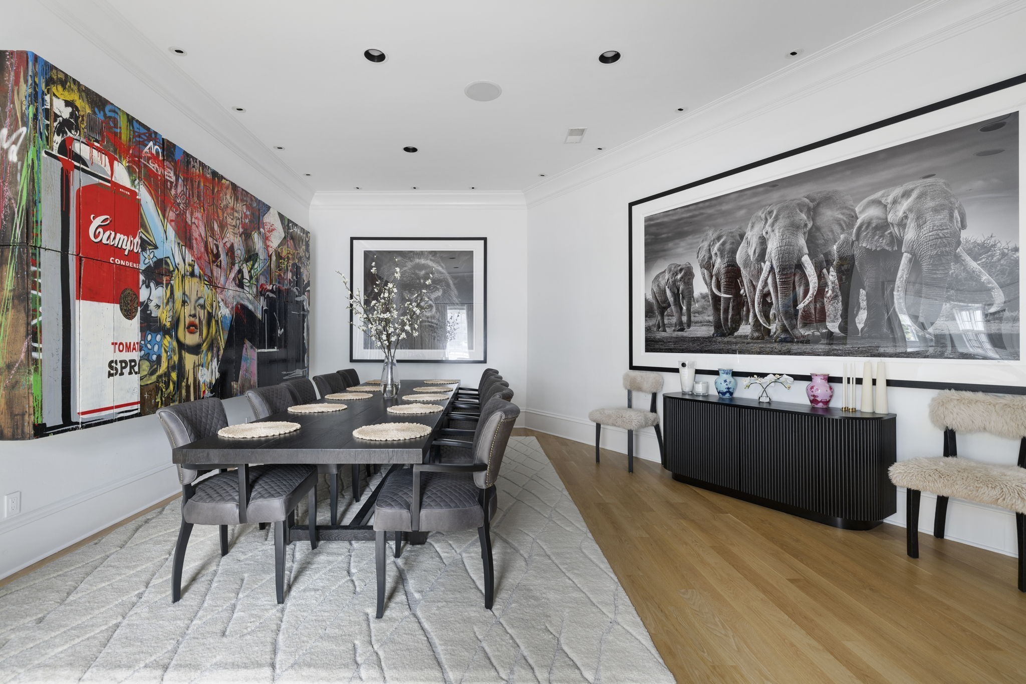 Dining room with a long dark table, colorful pop-art wall panels, and a large elephant photograph.