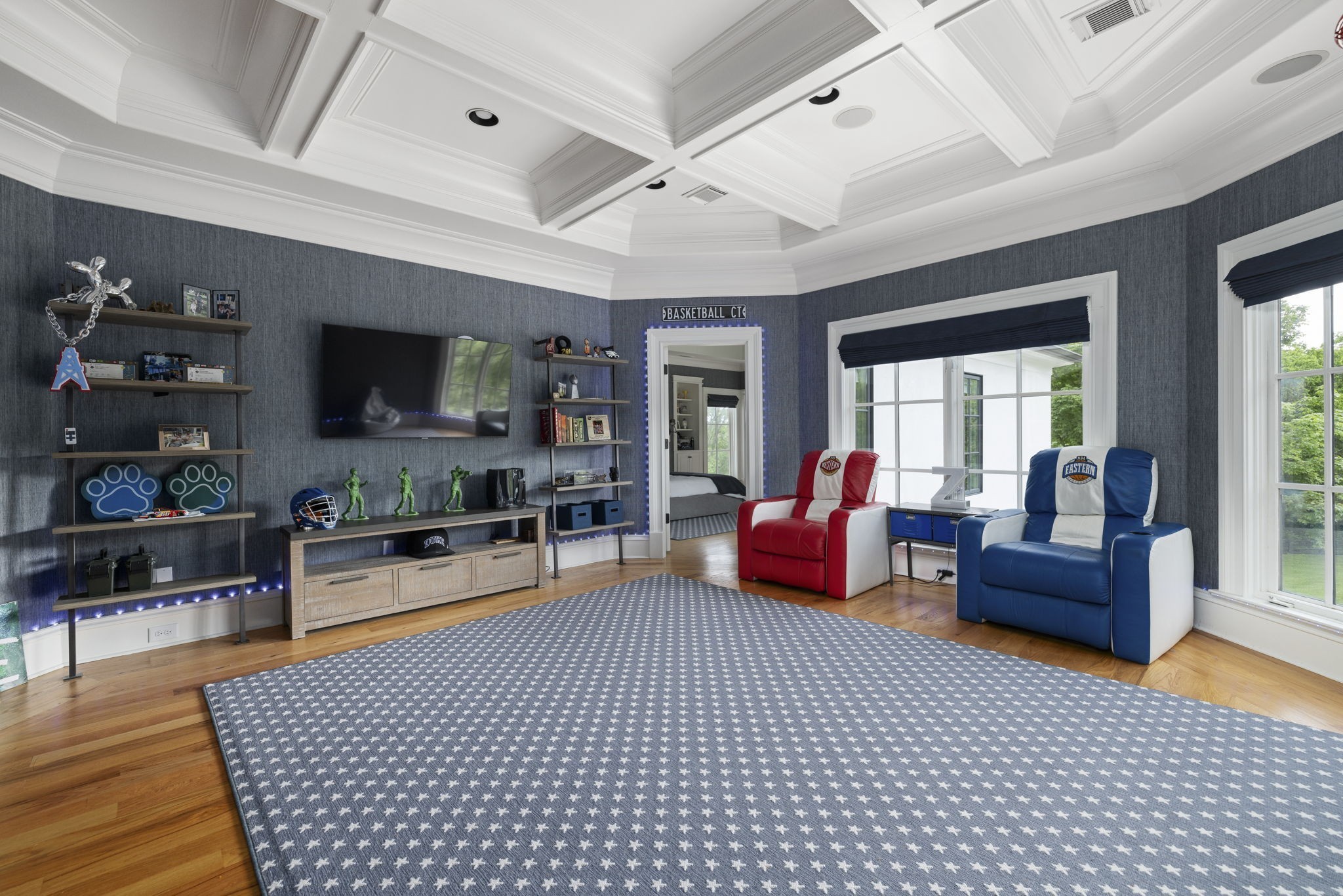 Media room with sports-themed recliners, memorabilia shelves, a coffered ceiling, and large windows.