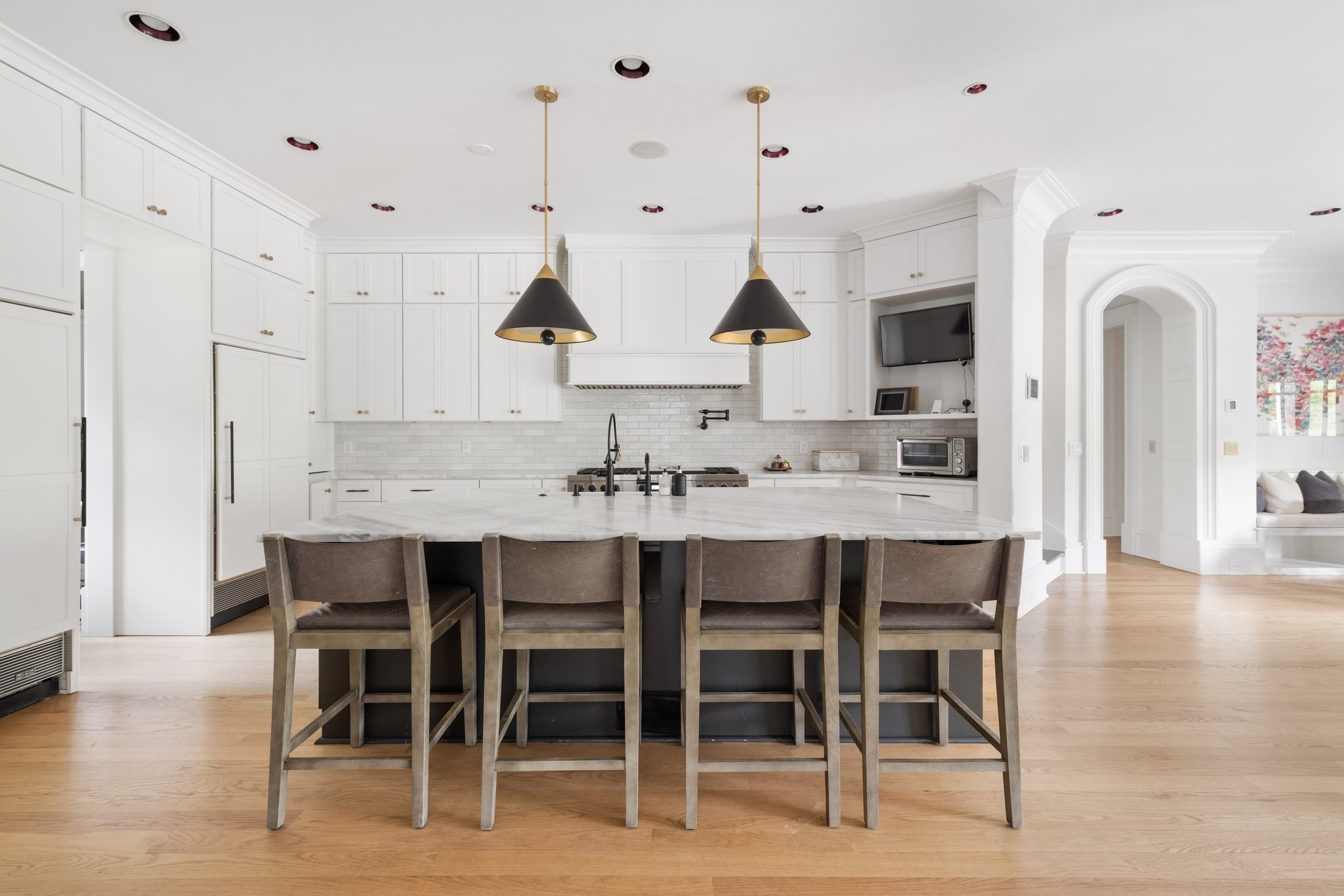 Bright white kitchen with a large marble island, four bar stools, and two pendant lights.