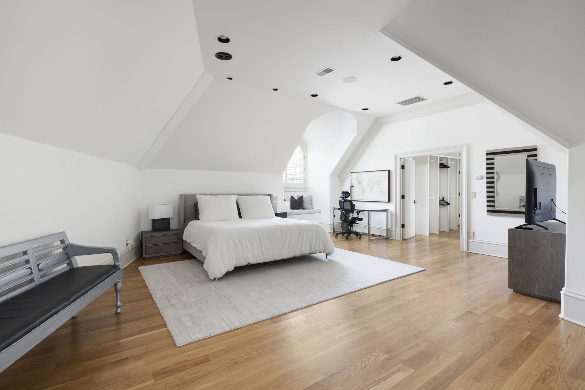 Attic bedroom with a white bed, sloped ceiling, hardwood floors, and an open closet.