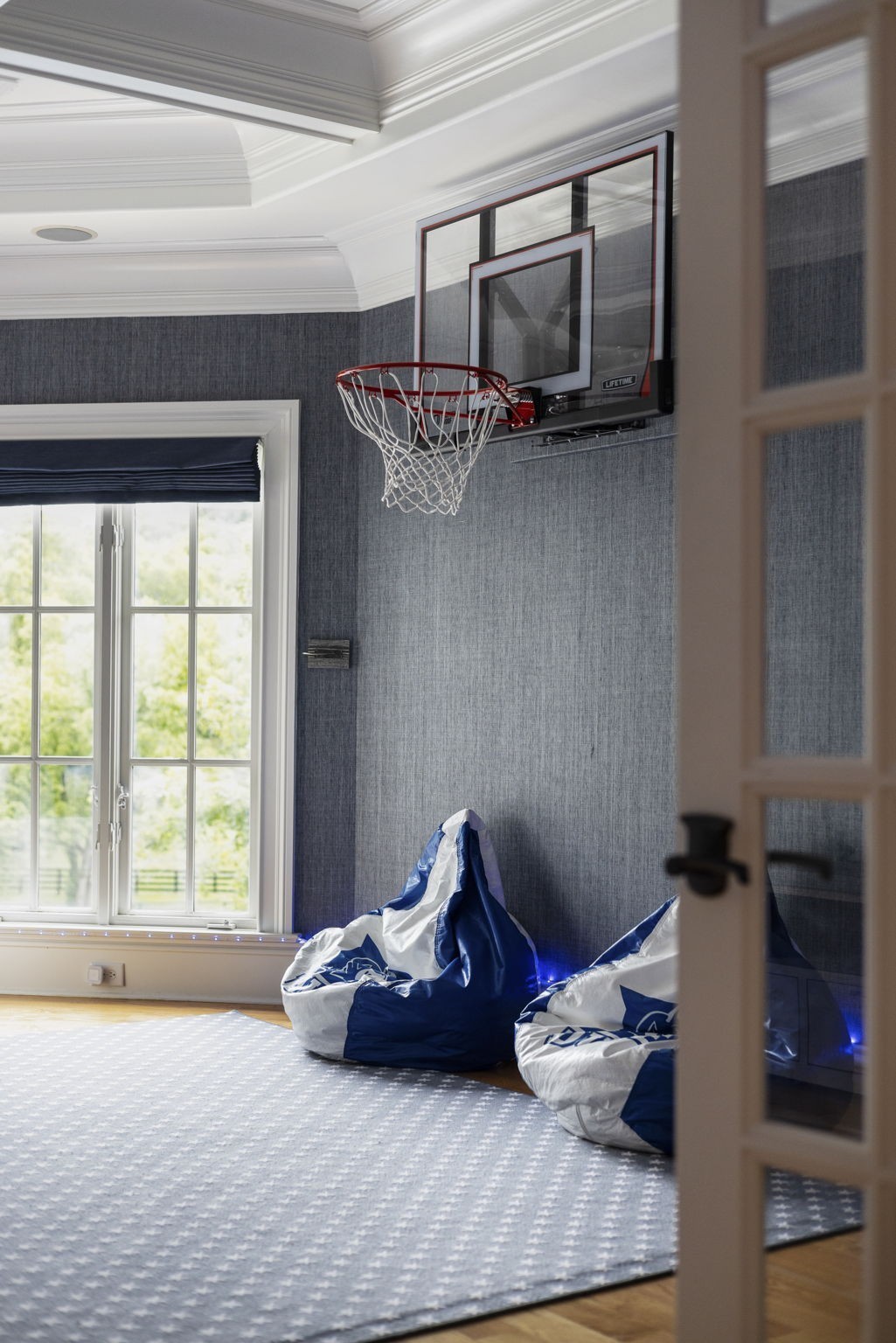 Game room with a wall-mounted basketball hoop, blue-and-white beanbag chairs, and a tall window.