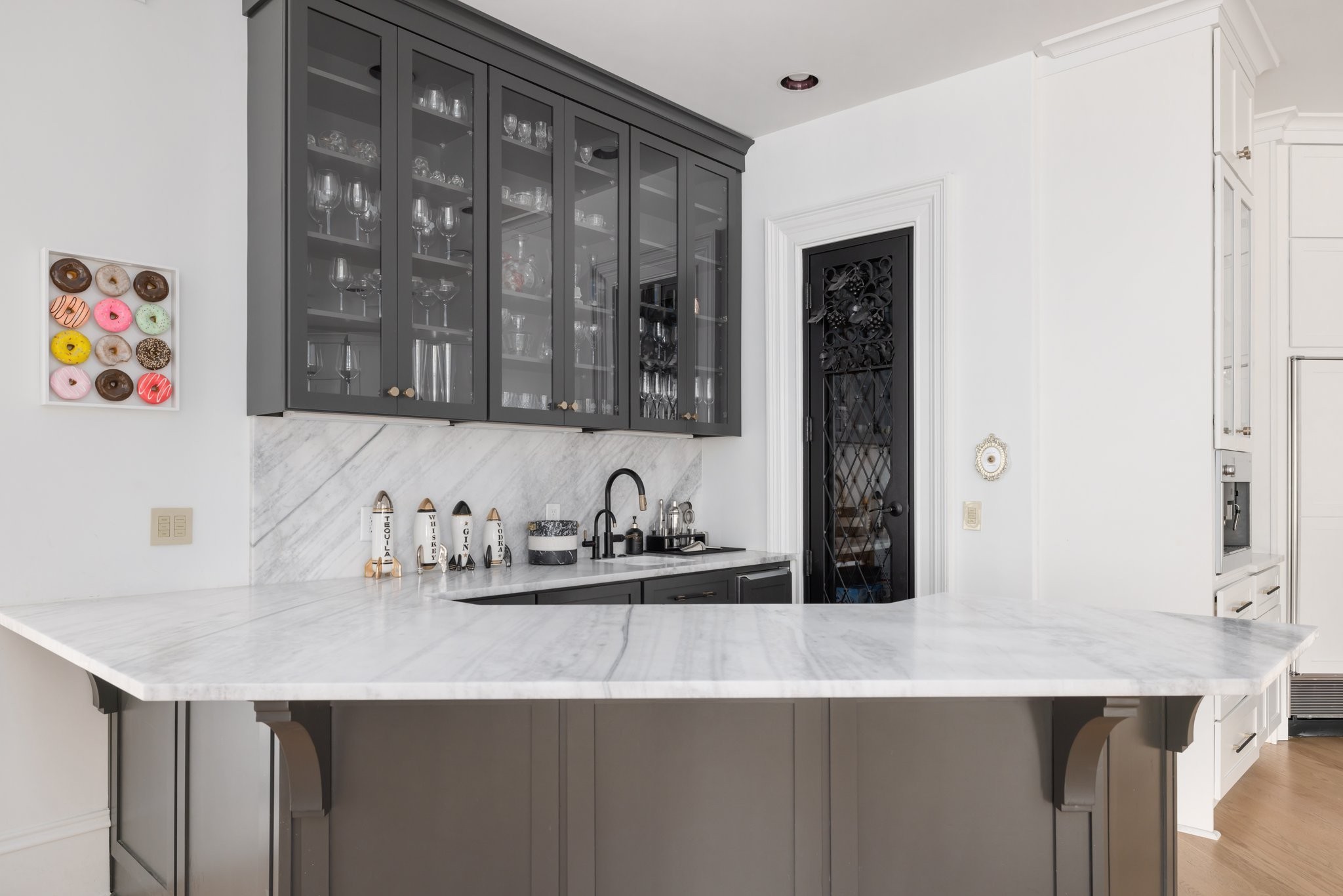 Kitchen beverage station with a marble island, dark glass-front cabinets, and a black lattice wine-cellar door.