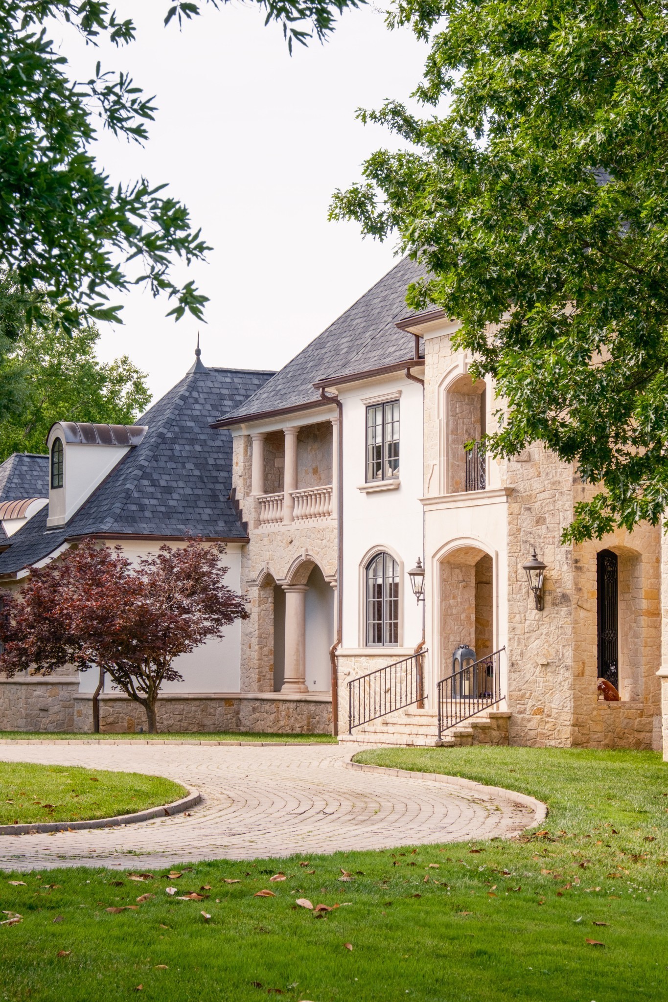Stone-and-stucco home with slate roofs, arched entryways, and a curved driveway.