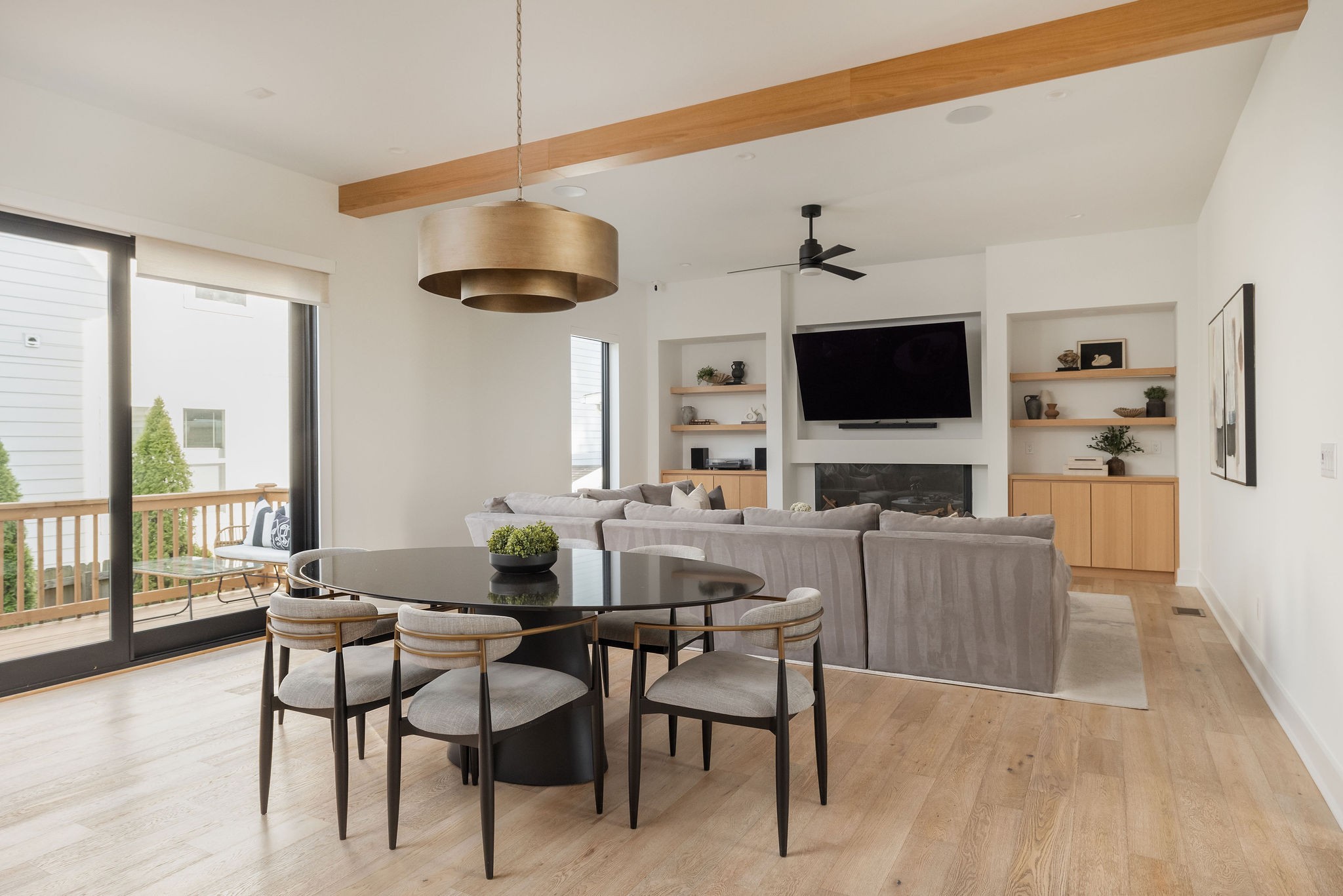 Open-plan living and dining room with a gray sectional, fireplace, built-in shelves, and sliding doors to a deck.