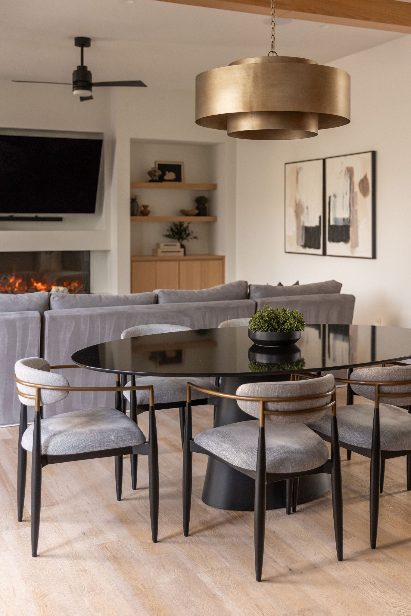Dining area with black oval table and gray chairs, opening onto a living room with a fireplace.