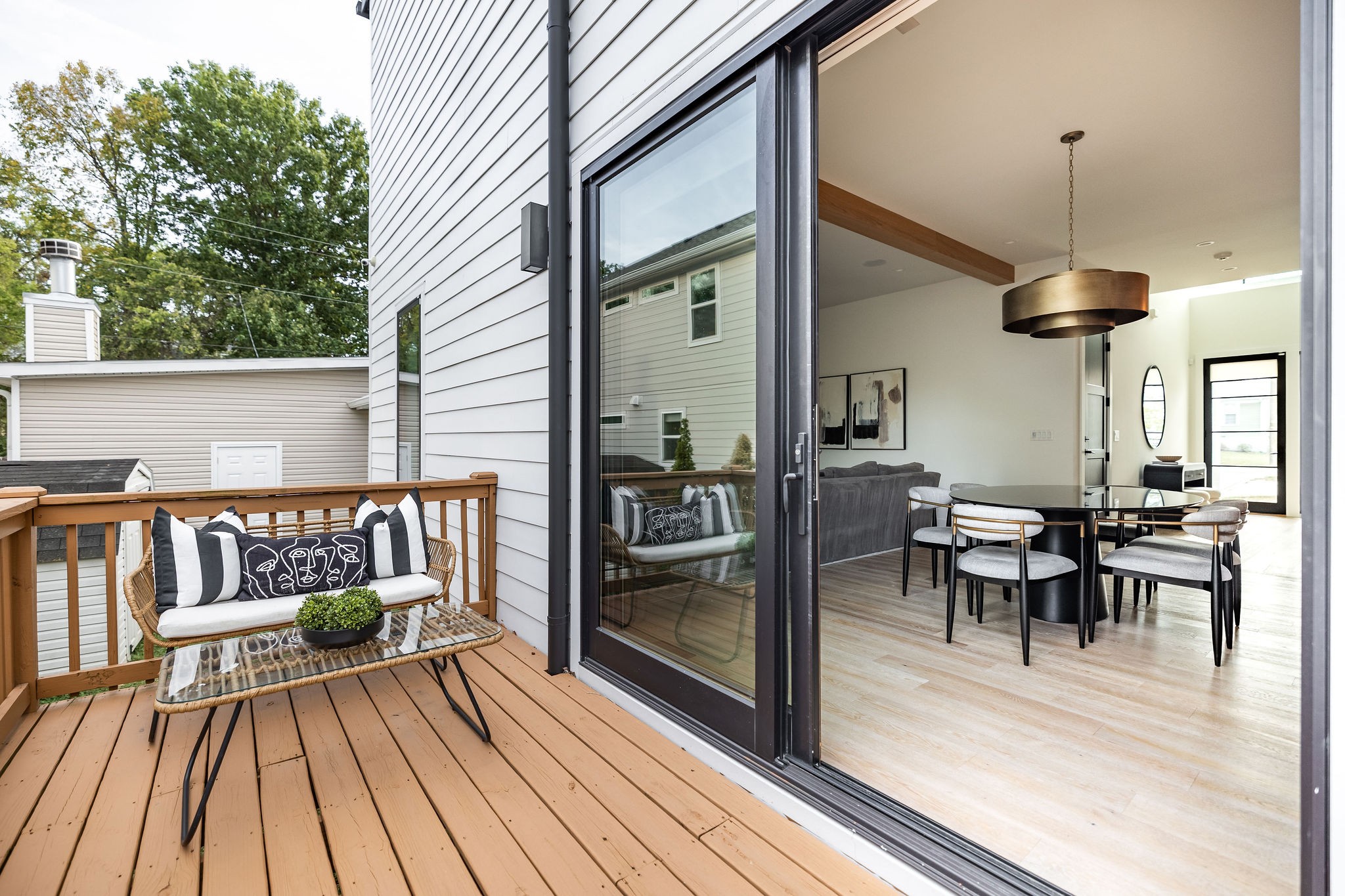 Wooden deck with wicker seating opens through sliding glass doors to a bright dining and living area.