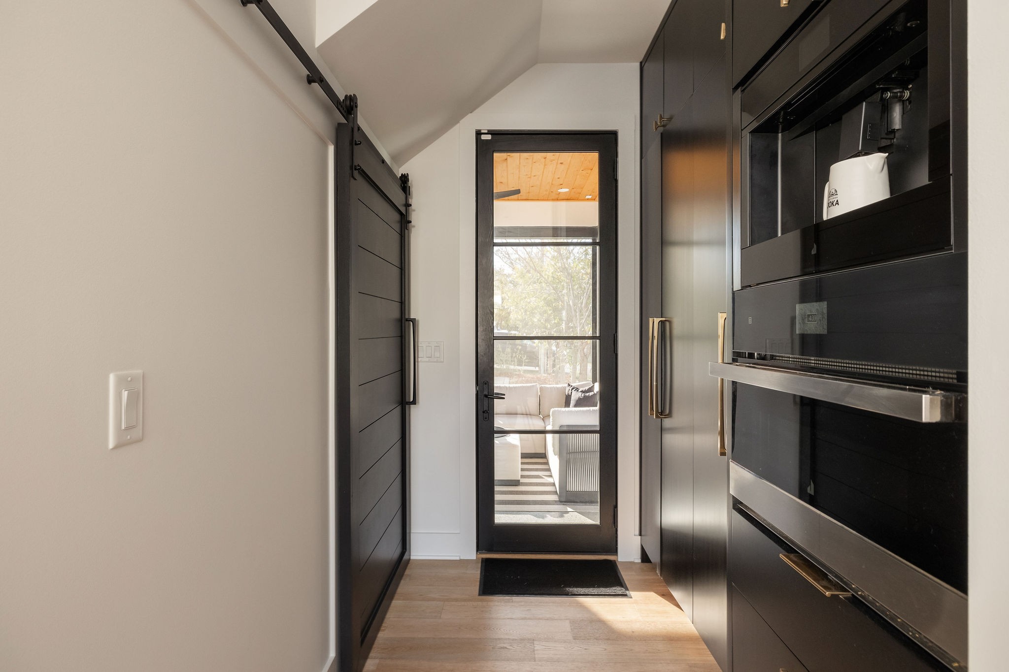 Kitchen entry with black cabinetry and built-in oven beside a glass door to the living area.