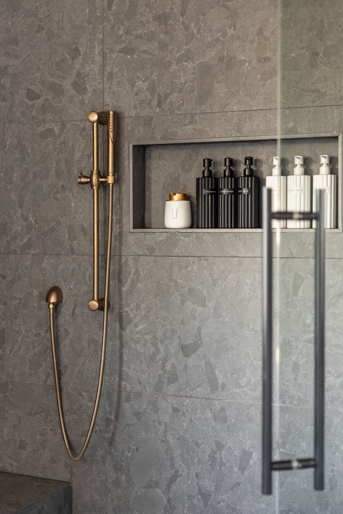 Stone-tiled shower with bronze fixtures and a recessed niche stocked with bath products.