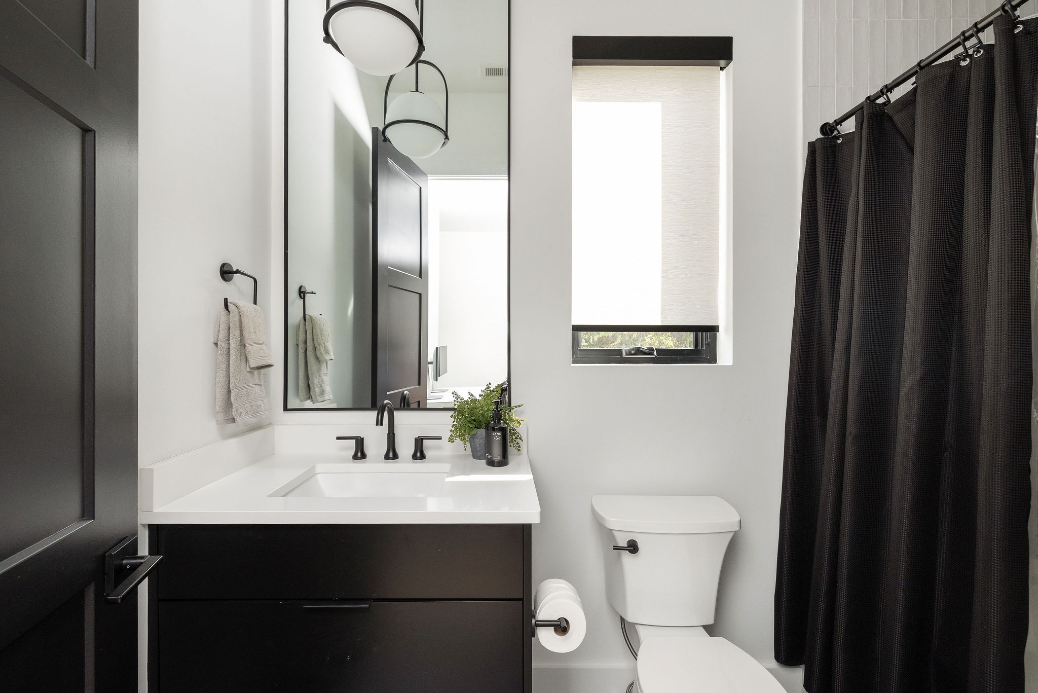 Modern bathroom with a dark vanity, large mirror, and black shower curtain.