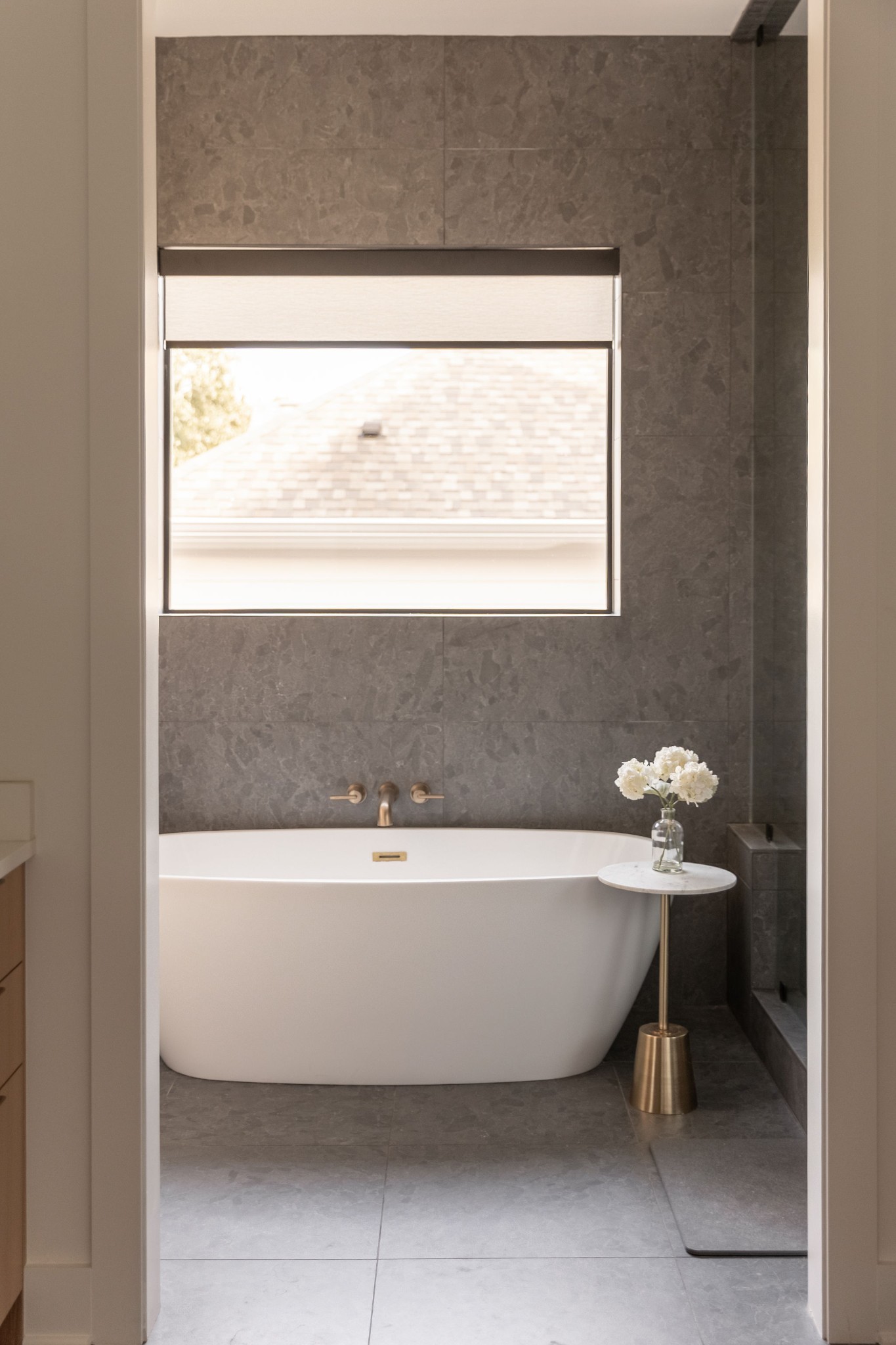 Bathroom with a freestanding tub, dark stone tile, brass fixtures, and a window above.