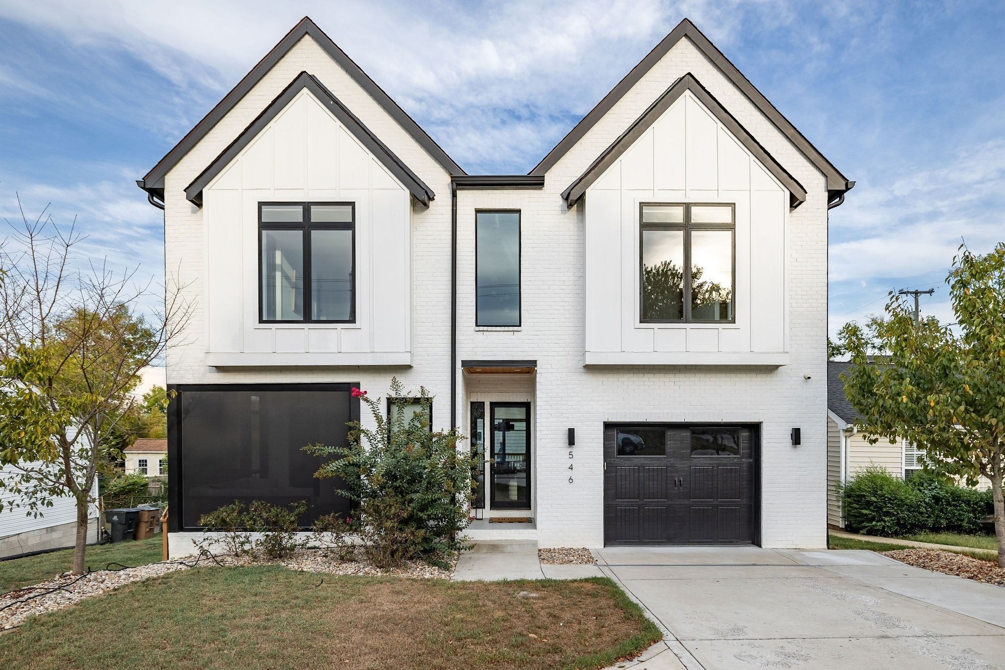 Modern white brick house with twin gables, black garage doors, and the number 546 beside the entrance.
