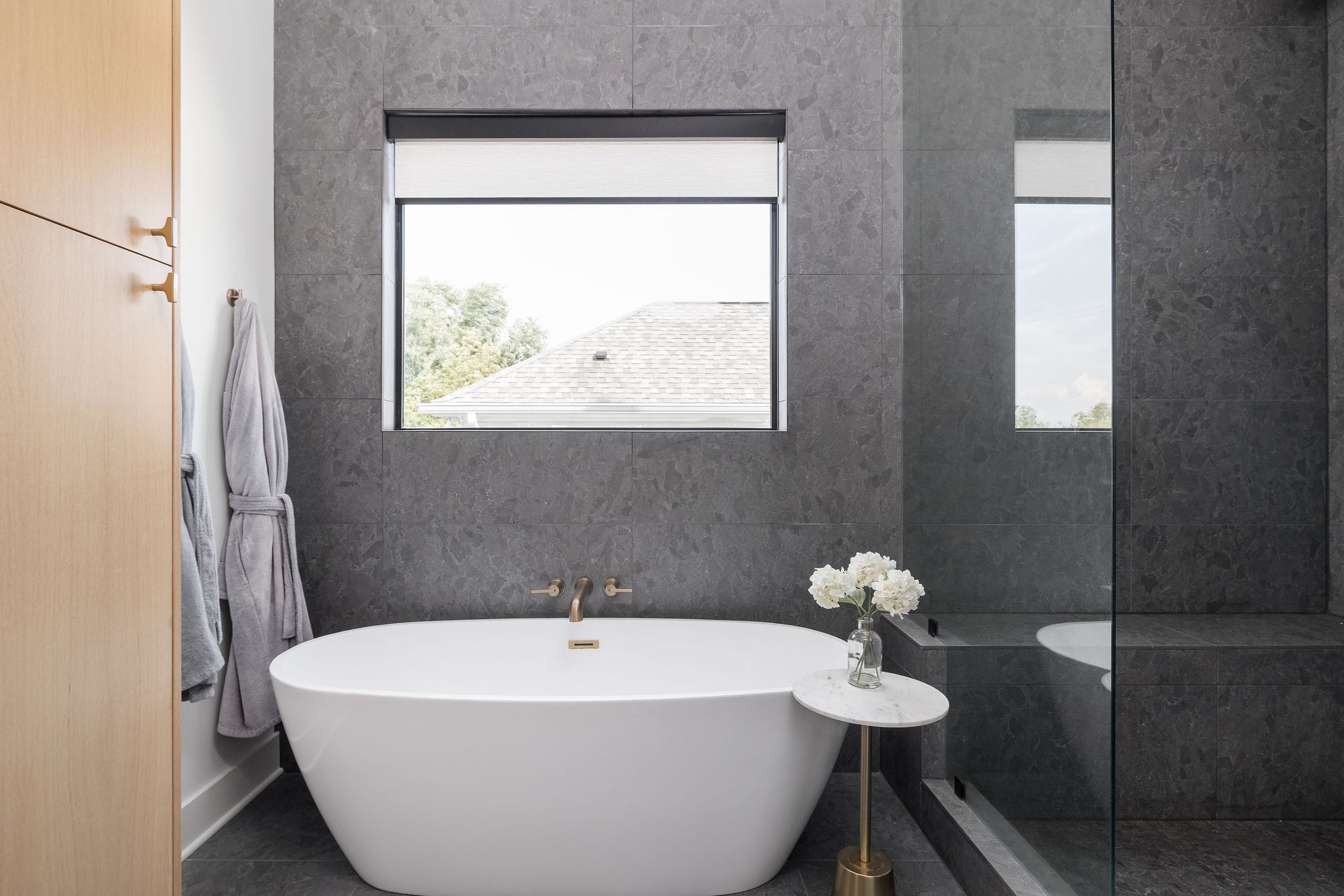 Modern bathroom with a freestanding soaking tub, dark stone tile, and glass-enclosed shower.