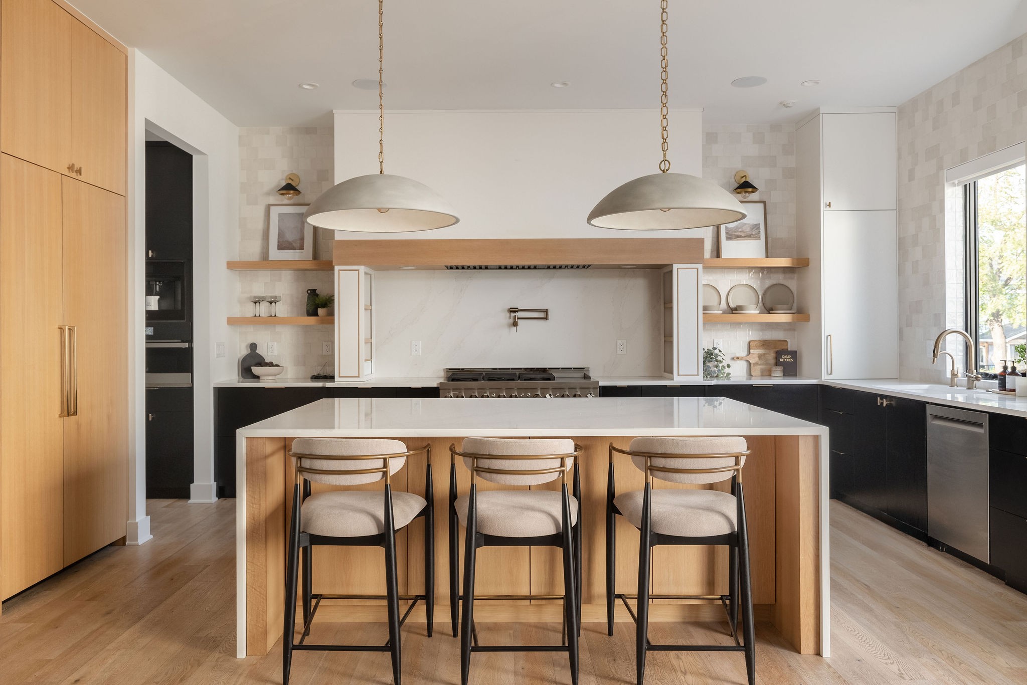 Modern kitchen with a large stone island, three counter stools, warm wood cabinetry, and pendant lights.
