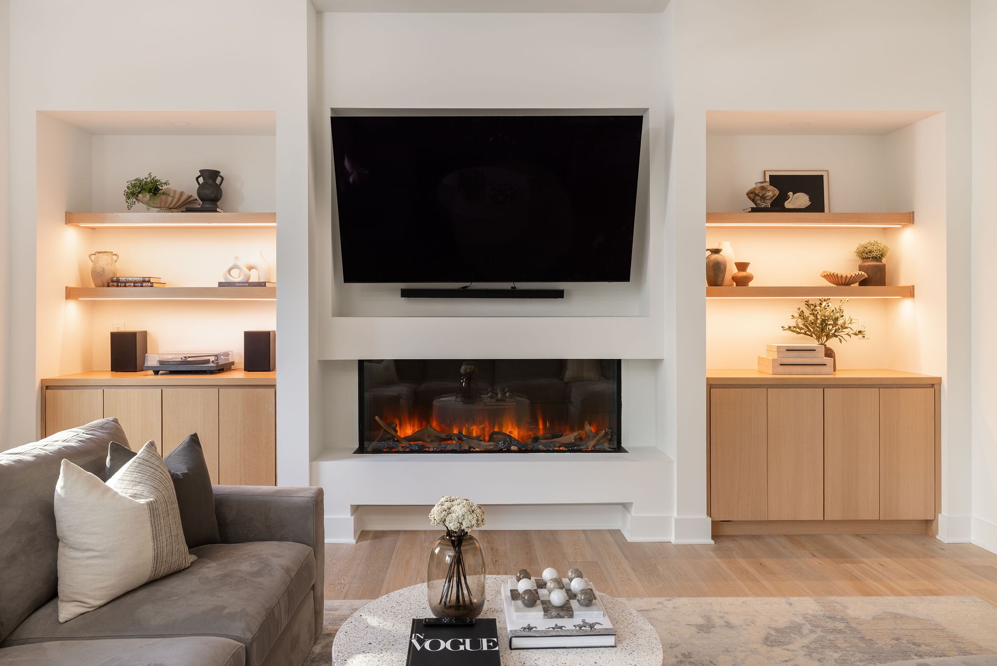 Living room with a gray sofa and wood built-ins framing a television and fireplace.