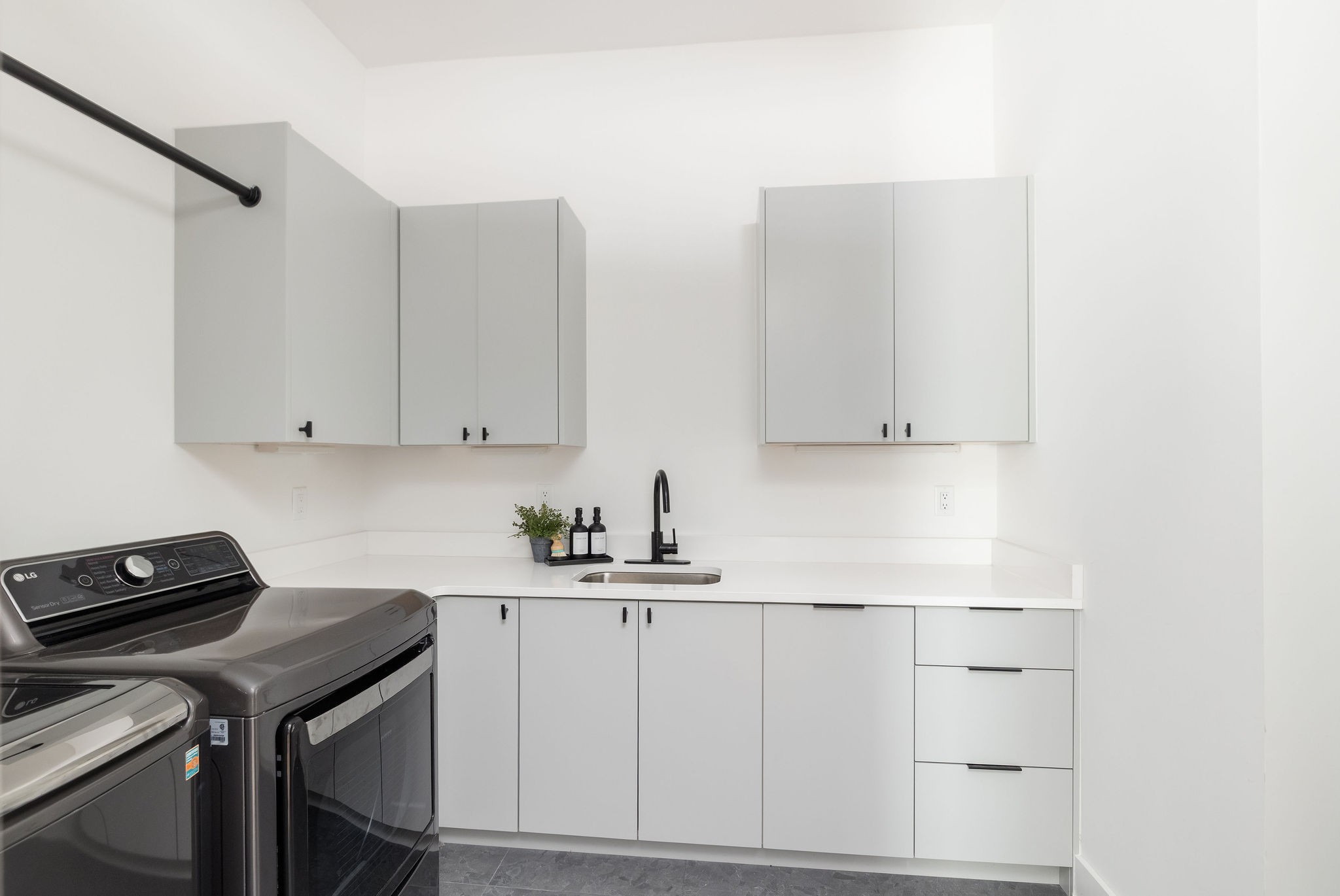 Laundry room with white cabinetry, a black faucet, and dark washer and dryer.