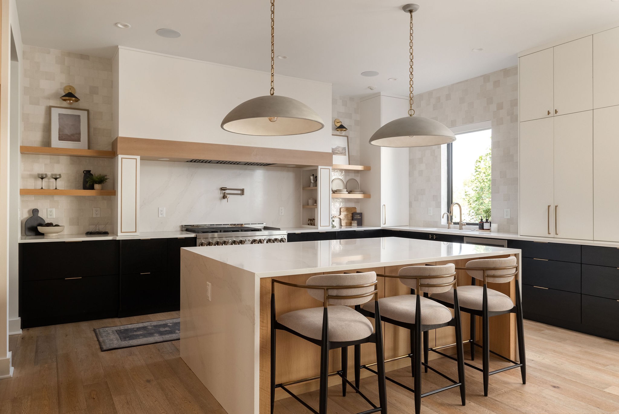 Modern kitchen with a white island, wood-paneled breakfast bar, three stools, and oversized pendant lights.