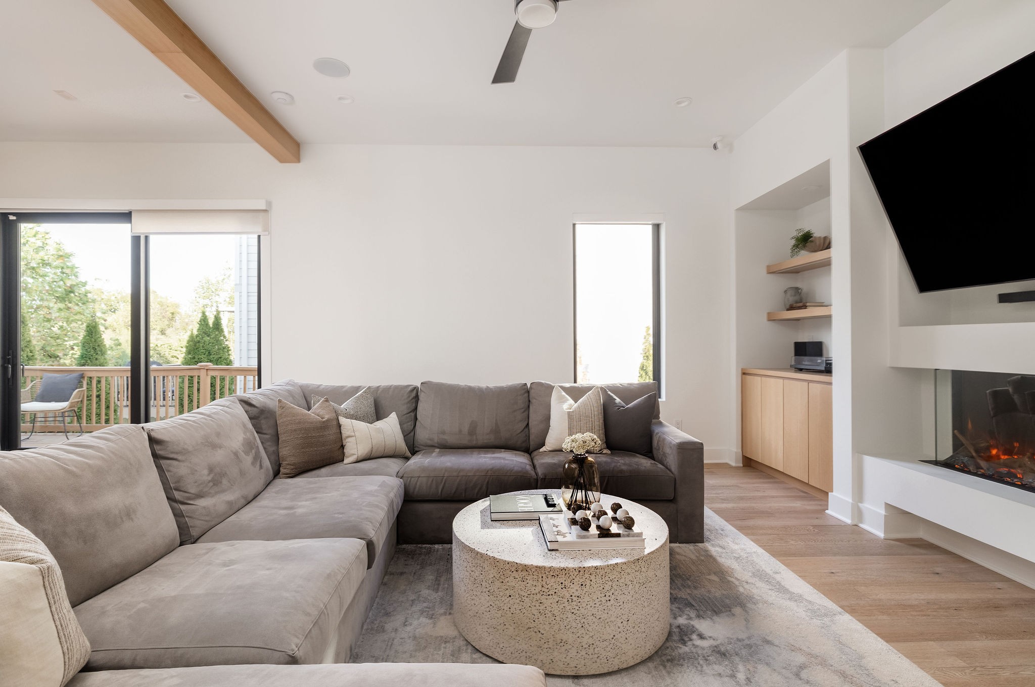 Living room with a gray sectional, modern fireplace, wood ceiling beam, and sliding doors to a deck.