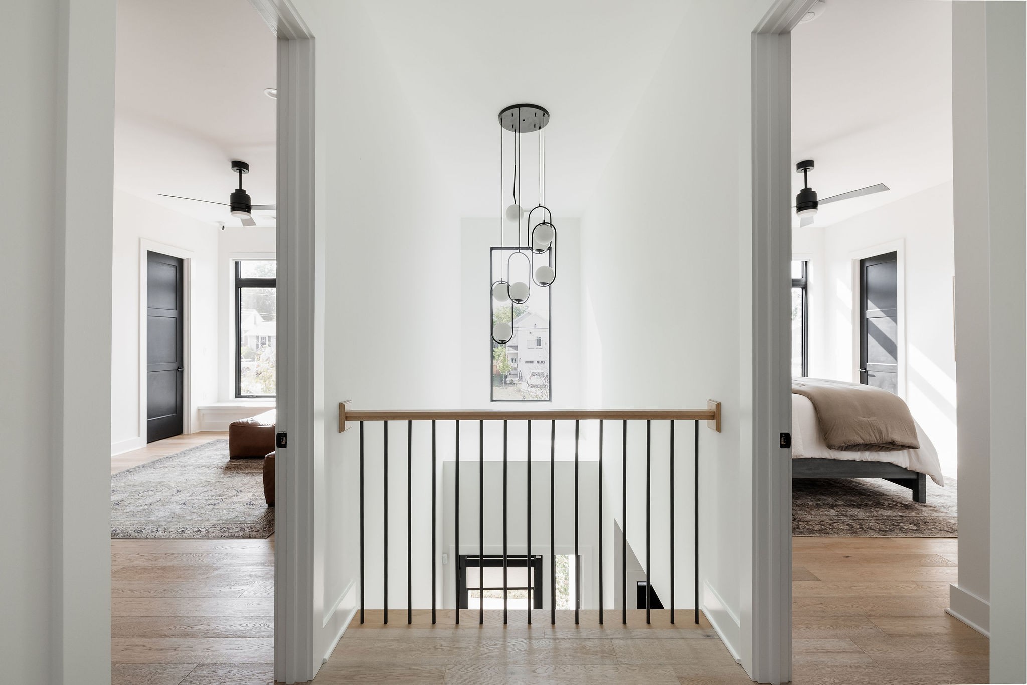 Upstairs landing with a black metal stair railing, modern pendant light, and bedrooms on either side.