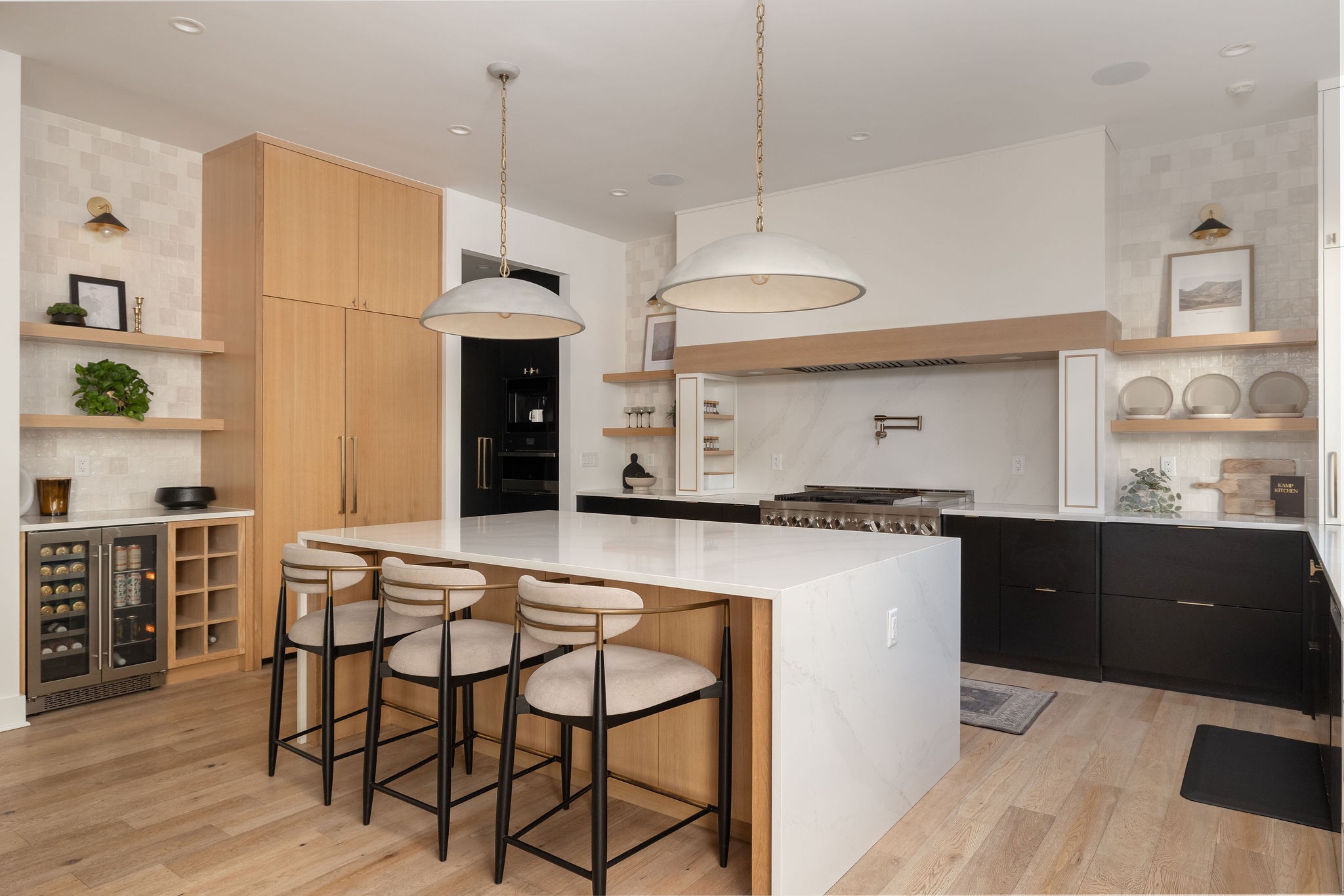 Contemporary kitchen with a large white island, three bar stools, light wood cabinetry, and black lower cabinets.