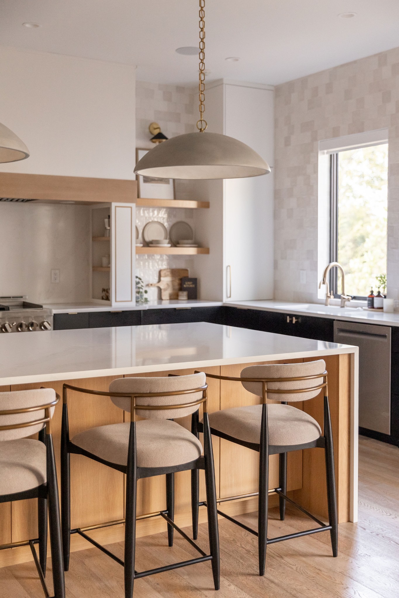 Modern kitchen with a white island, three upholstered bar stools, and a large window above the sink.