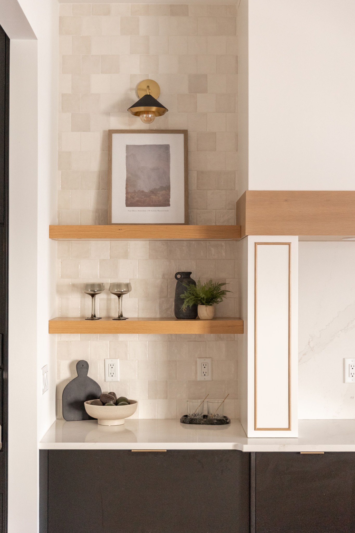 Kitchen with cream tile backsplash, floating oak shelves, dark cabinets, and white stone countertop.
