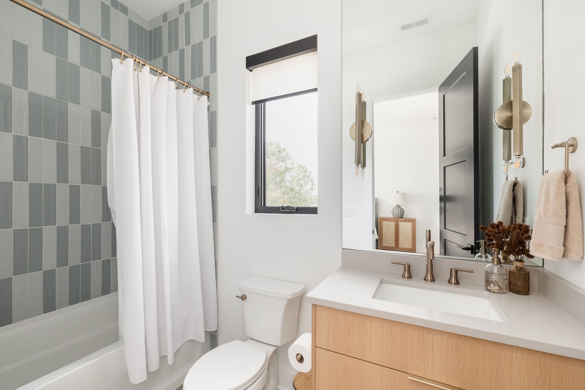 Bathroom with gray tiled tub, white shower curtain, and light wood vanity with brass fixtures.