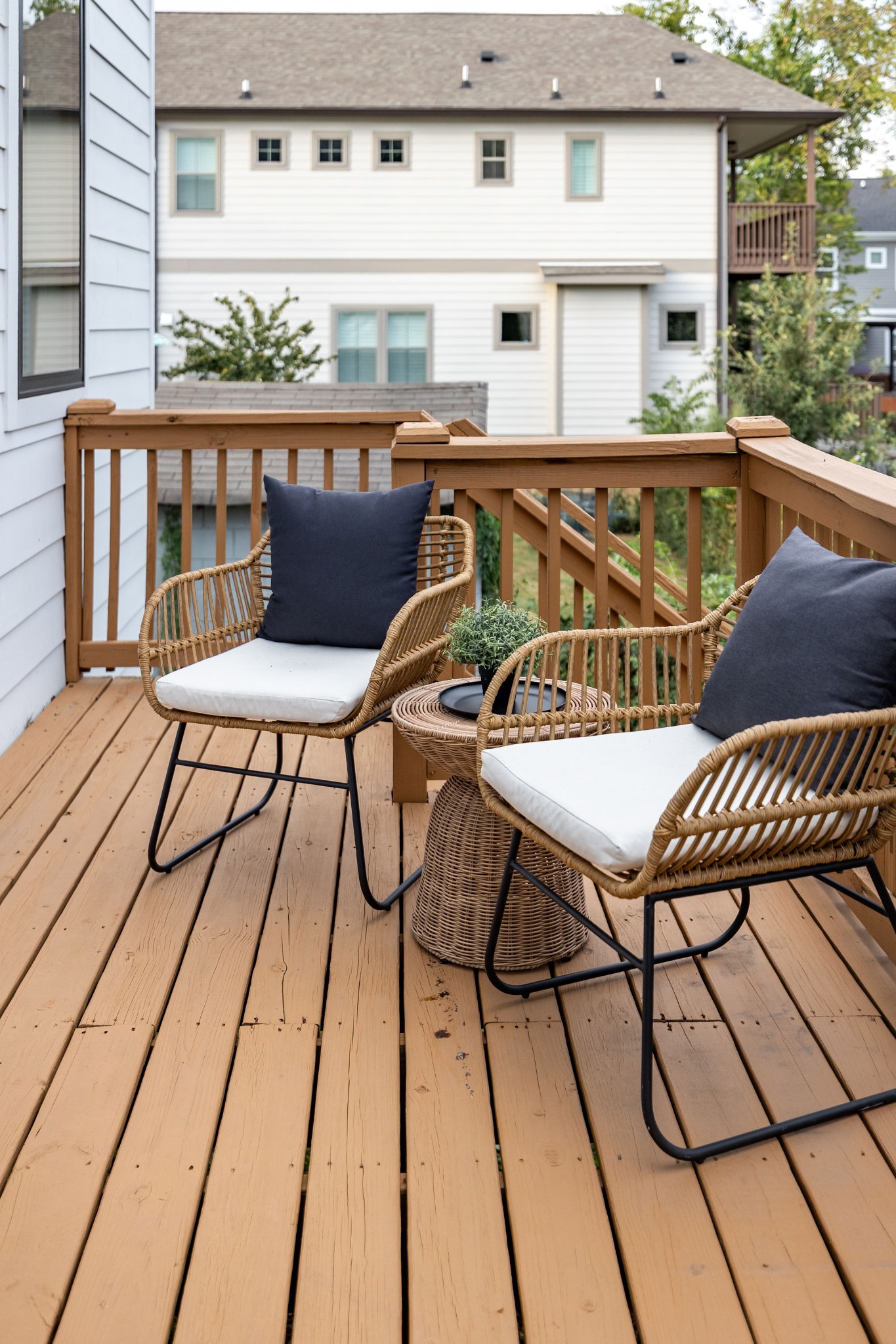Wooden deck furnished with two wicker chairs and a small table, overlooking neighboring homes.