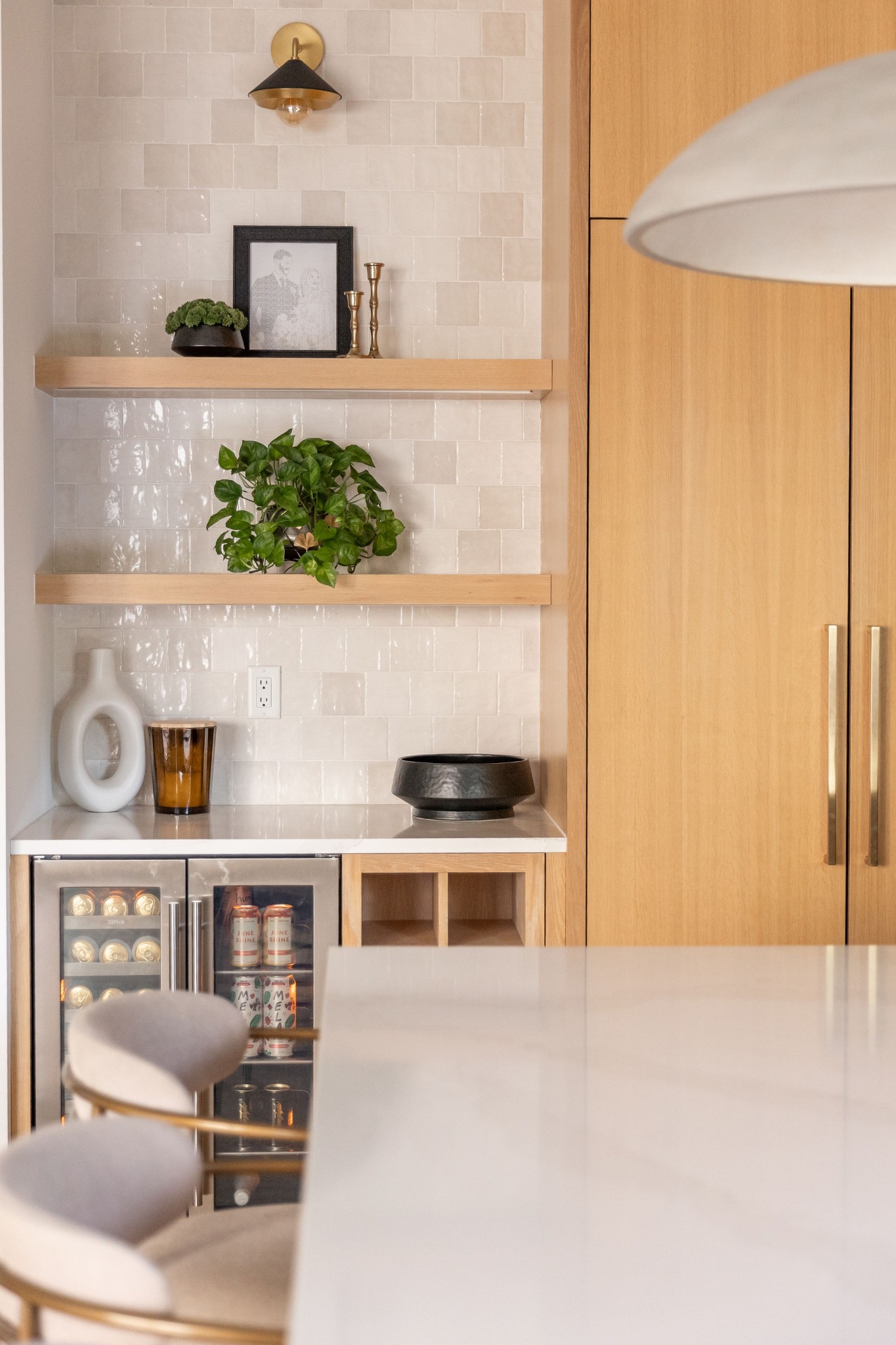 Kitchen bar with white tile backsplash, floating oak shelves, and glass-front beverage refrigerator.