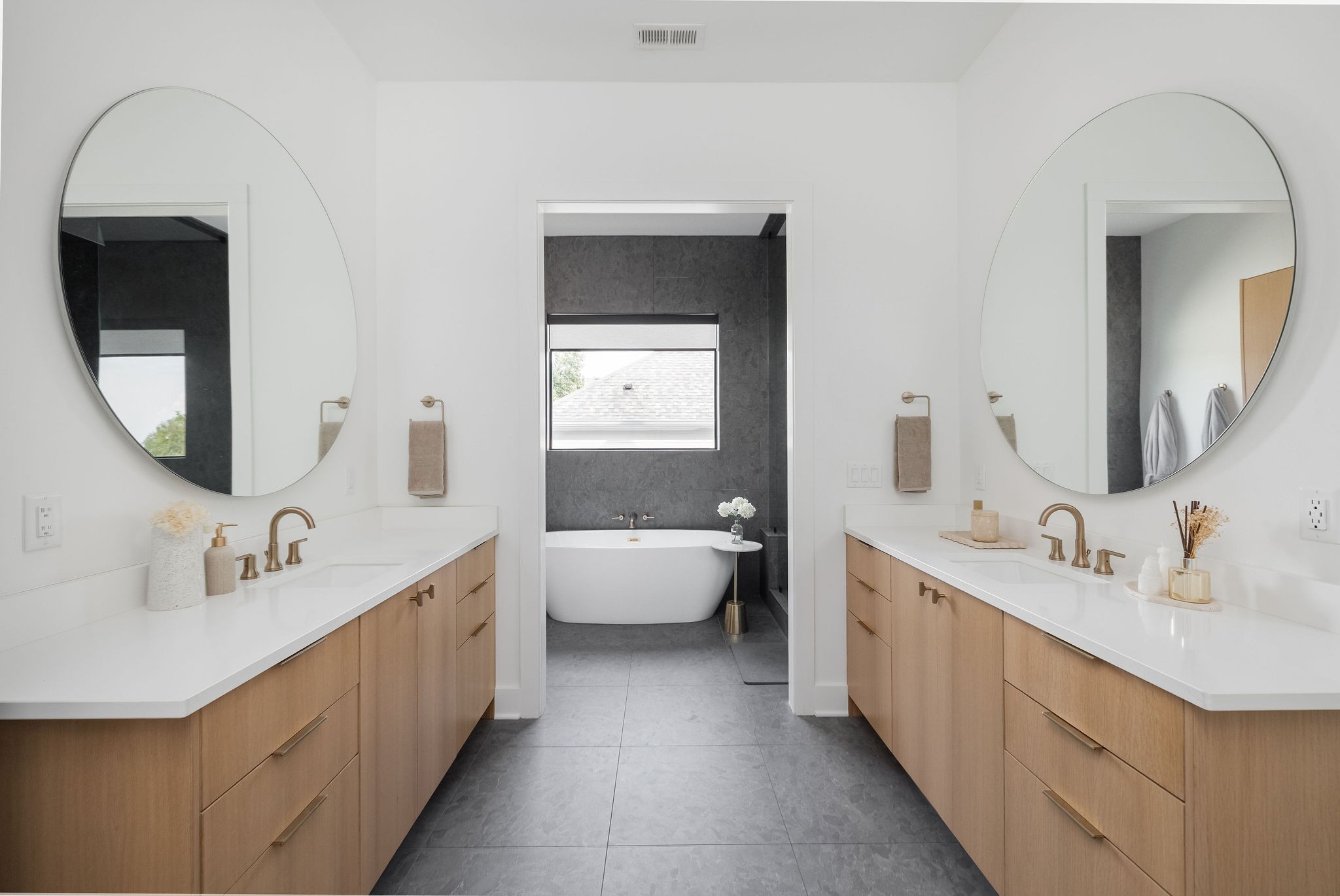Bathroom with double wood vanities and oval mirrors framing a freestanding tub.