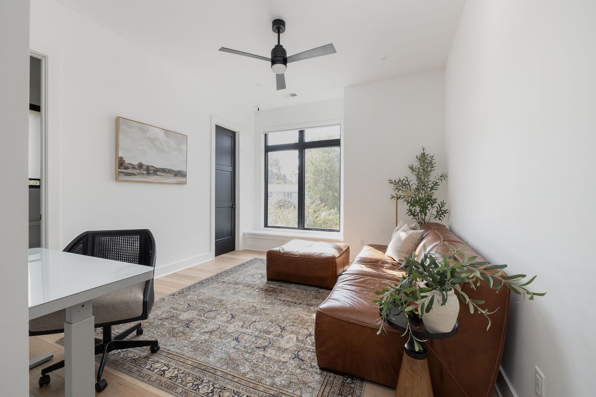 Living room with a brown leather sofa, patterned rug, and large black-framed window.