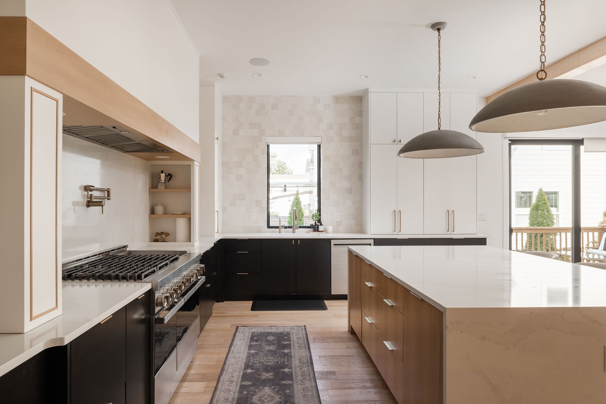 Modern kitchen with a large wood-paneled island, professional gas range, and oversized pendant lights.