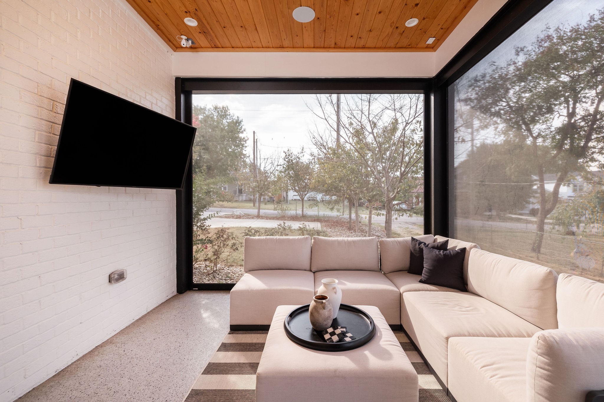Living room with a cream sectional, wood-plank ceiling, and large windows overlooking trees.