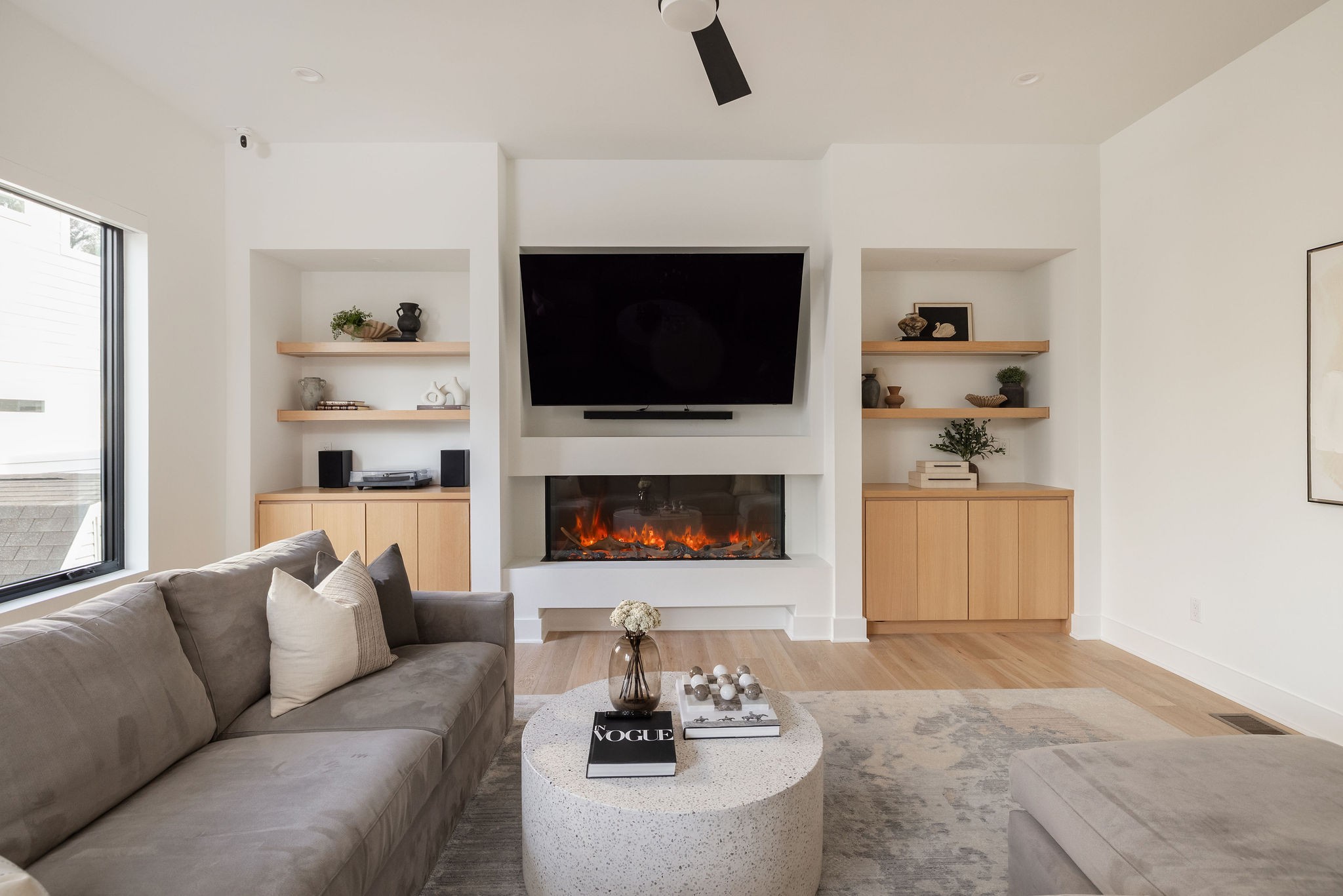 Living room with a gray sectional, built-in shelves, and a fireplace beneath a large television.
