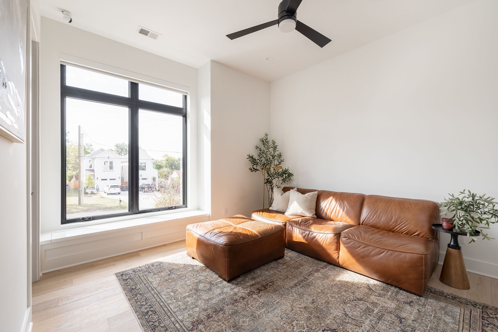 Living room with a cognac leather sectional, patterned rug, and large black-framed windows.