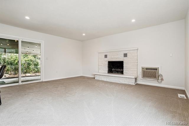 Empty living room with a white brick fireplace, carpet, and sliding glass doors.