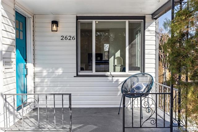 White-sided house porch with a bright blue door, black railings, and the number 2626.
