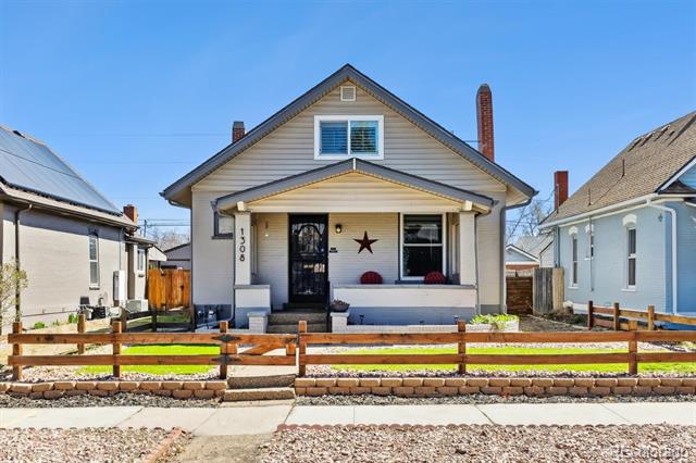 Small gabled house with a covered porch, black front door, and low wooden fence.