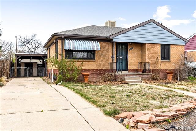 Brick house with a blue gable, striped awning, and driveway leading to a covered carport.