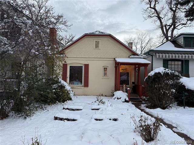 Cream-colored house with red trim and a covered entry porch, surrounded by snow.