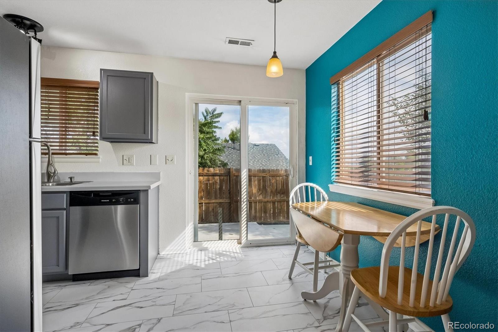 Kitchen and dining nook with turquoise wall, wood table, and sliding doors to a fenced patio.