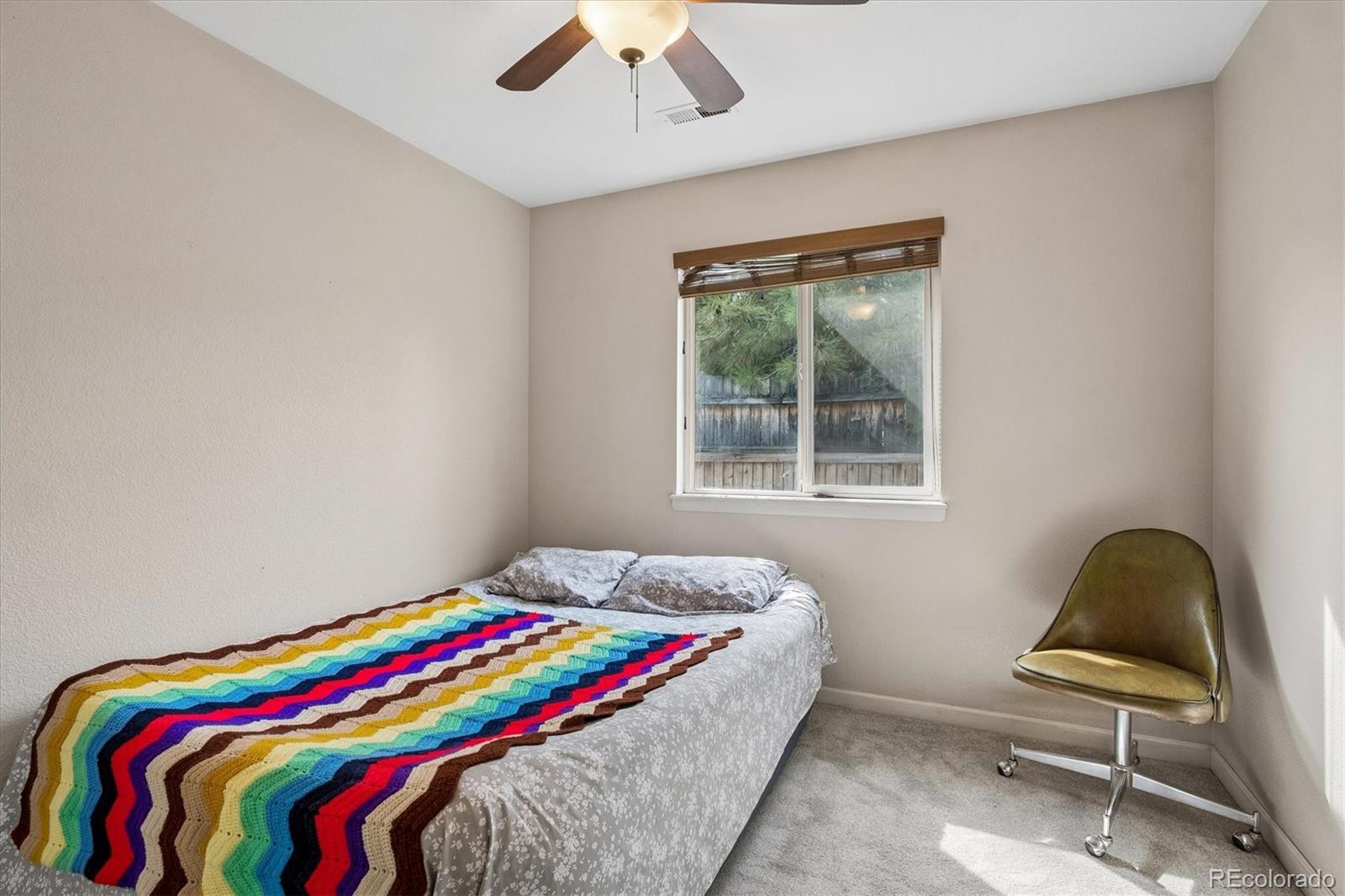 Bedroom with a bright multicolored blanket on the bed and an olive-colored chair by the window.
