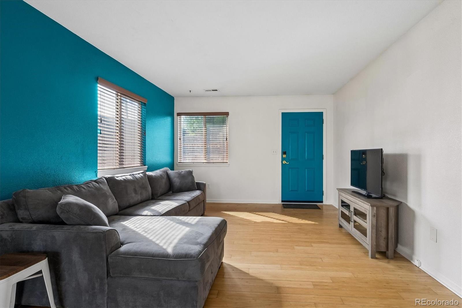 Living room with a gray sectional, teal accent wall, blue door, and hardwood floors.