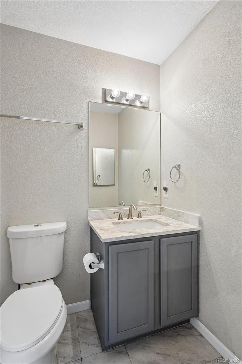 Bathroom with a gray vanity, marble-look countertop, large mirror, and white toilet.