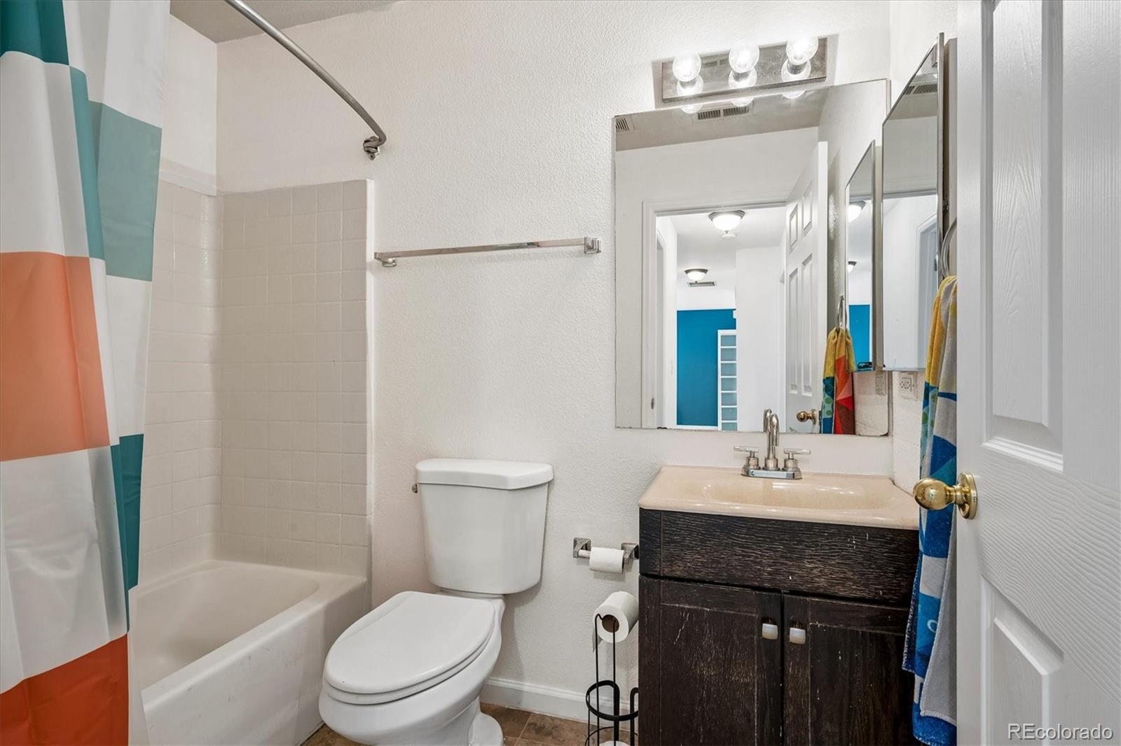 Bathroom with a striped shower curtain, white tub and toilet, and dark wood vanity.