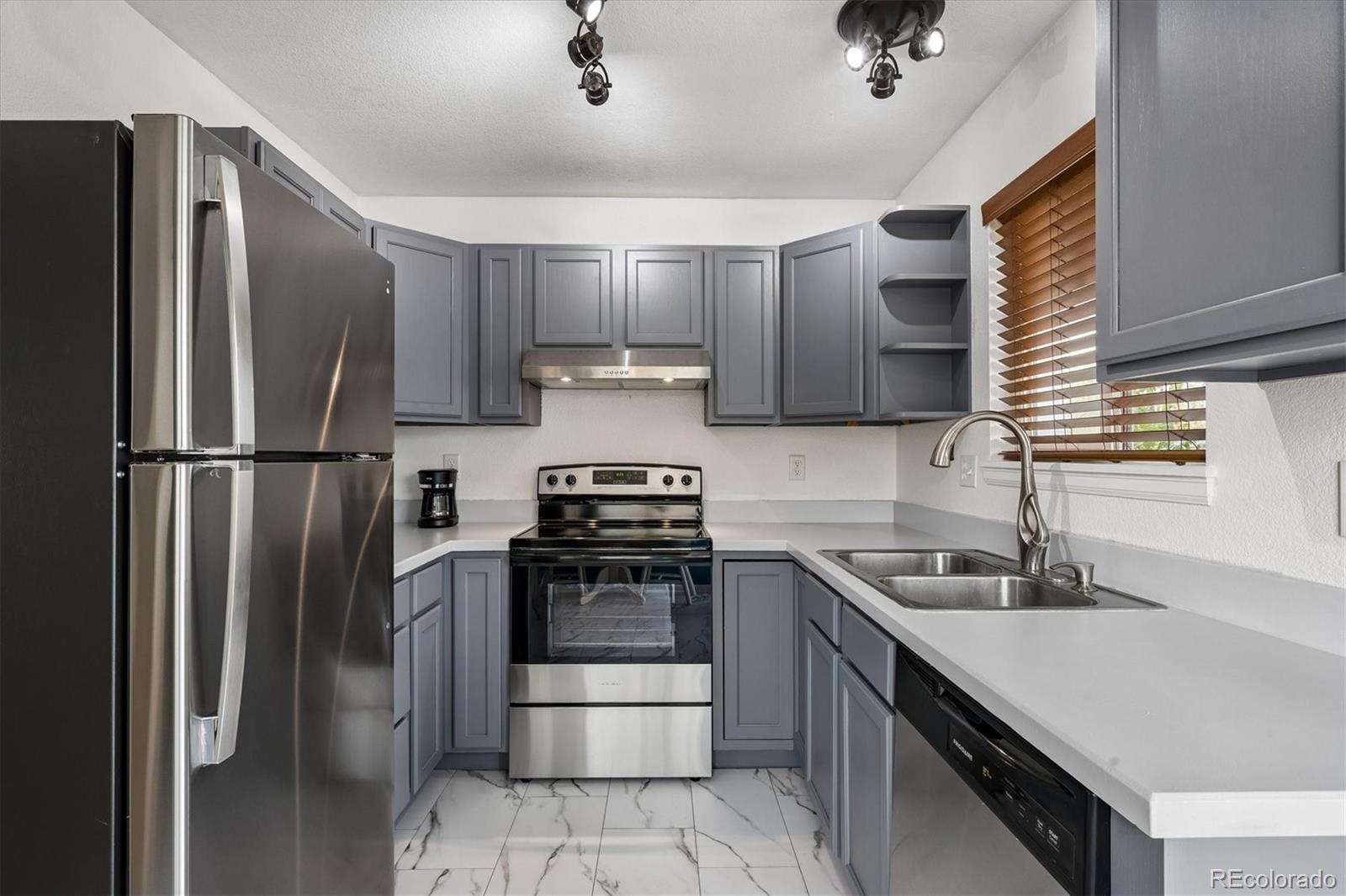 Kitchen with gray cabinets, stainless steel appliances, white counters, and marble-look tile flooring.